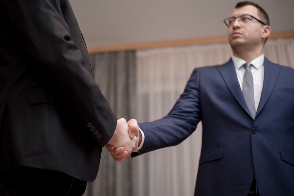 Business professionals completing acquisition deal with handshake in modern conference room